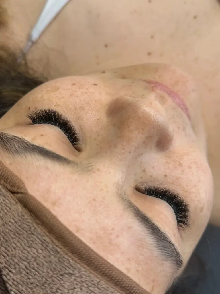 Close-up of closed eyes with full, curled lash extensions and neatly shaped eyebrows.