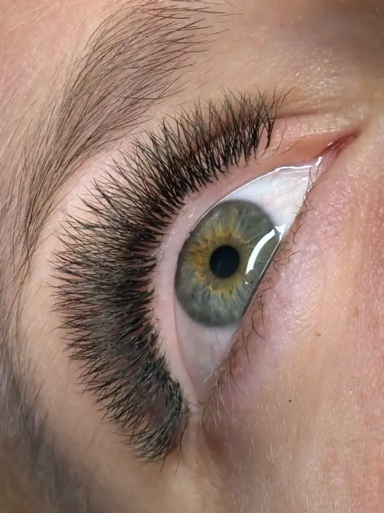 Close-up of a green-hazel eye with long, full black lash extensions and a natural brow.