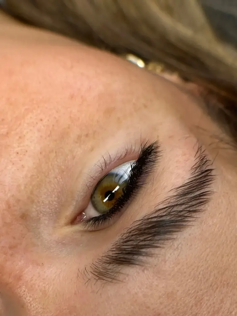 Close-up of a hazel eye with long curled lashes and a neatly shaped eyebrow.