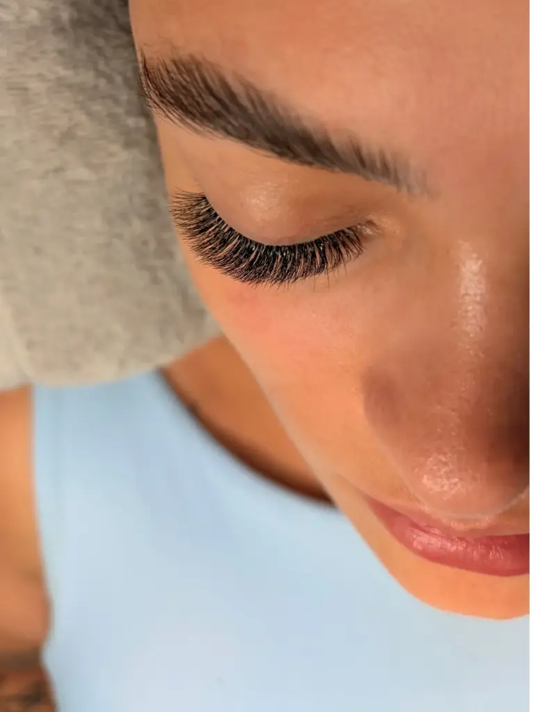 Close-up of a closed eye with full black lash extensions and a neatly shaped eyebrow