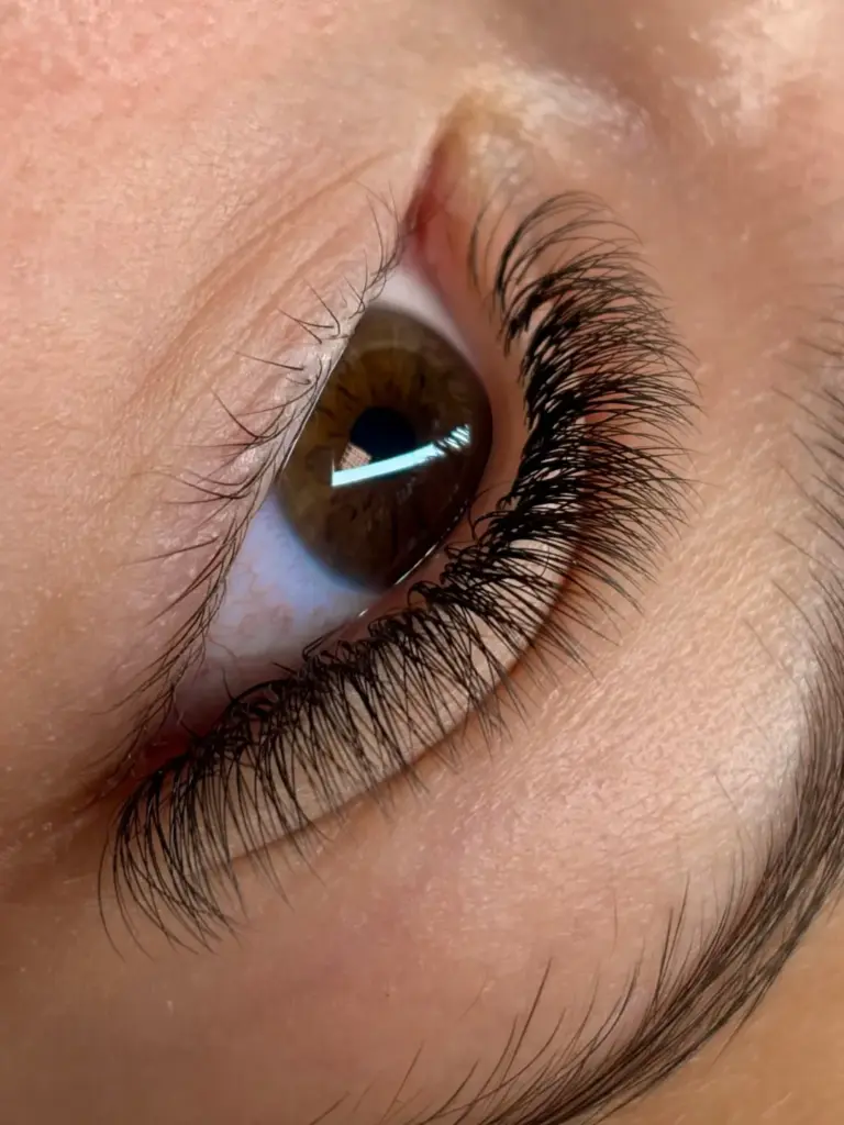 Close-up of a brown eye with long, dark, curled upper eyelashes and natural lower lashes.