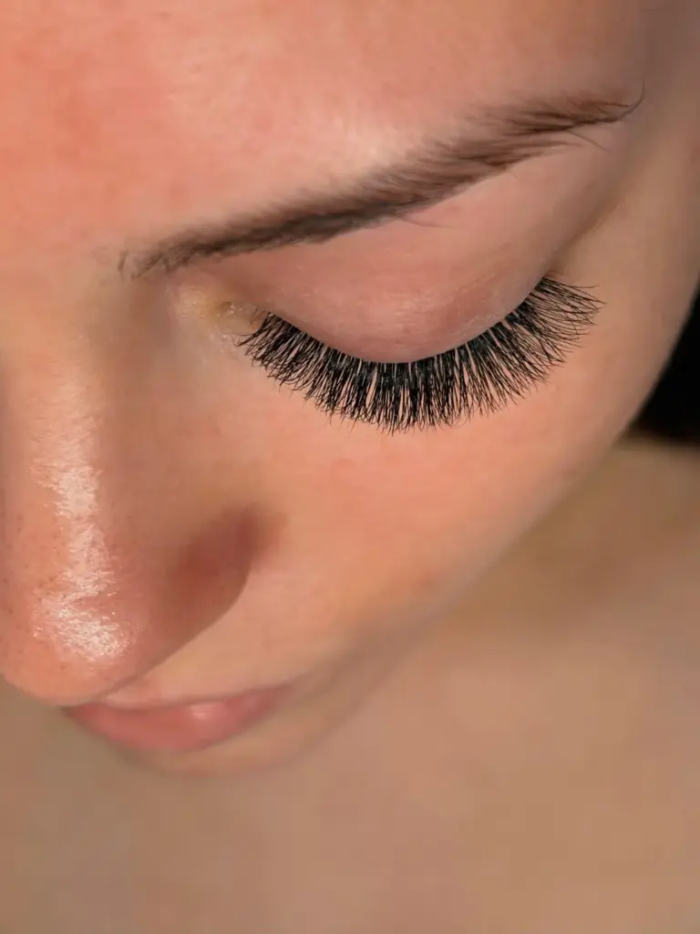 Close-up of a woman with her eye closed, showing long, dense black eyelash extensions and a shaped eyebrow.