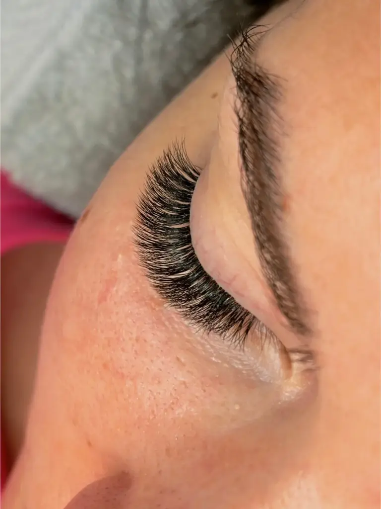 Close-up of a closed eye with dense, curled black lash extensions and a shaped eyebrow